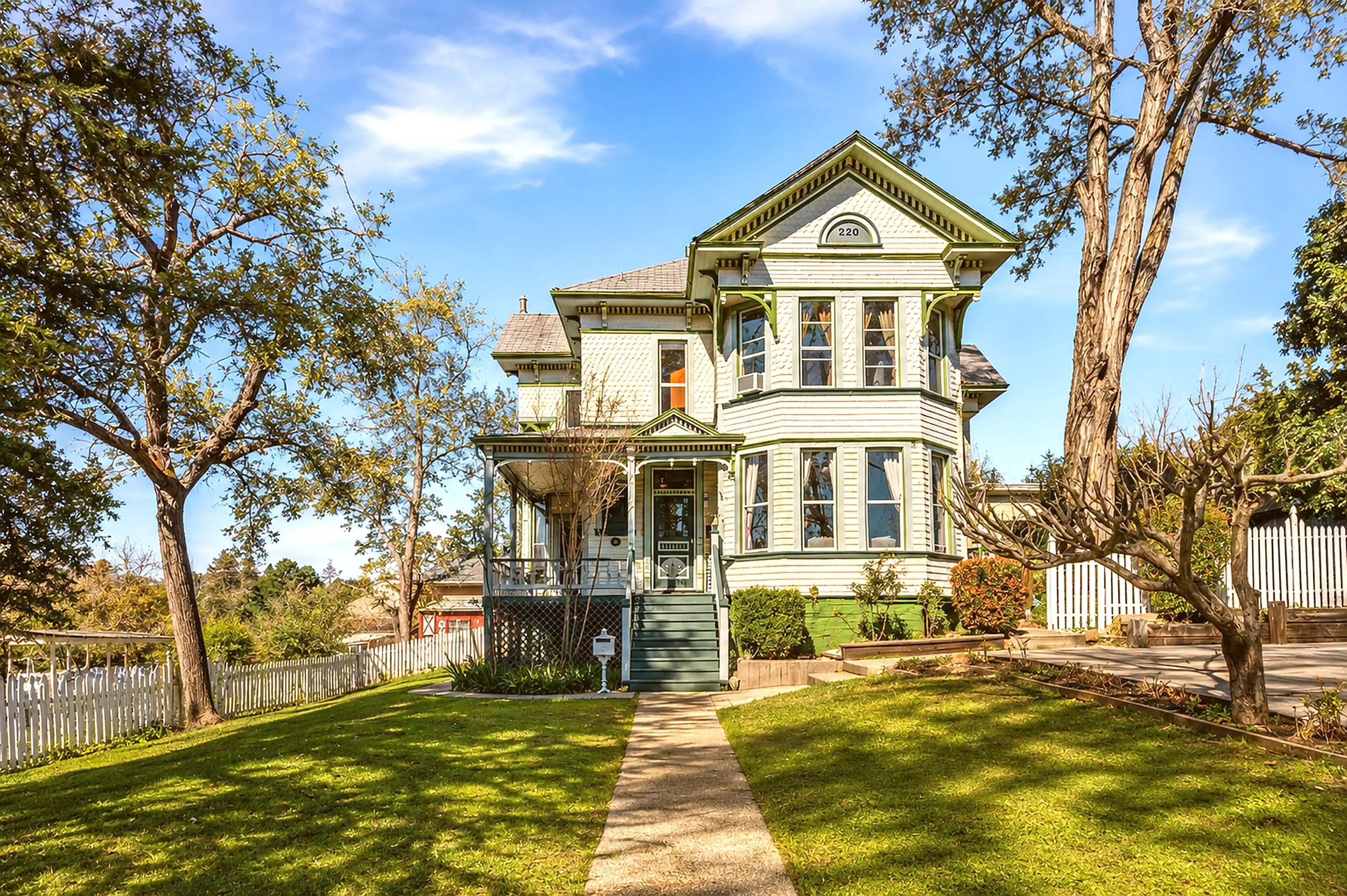 220 Colfax Avenue: a pale green Queen Anne Victorian with a wraparound porch, behind a white picket fence